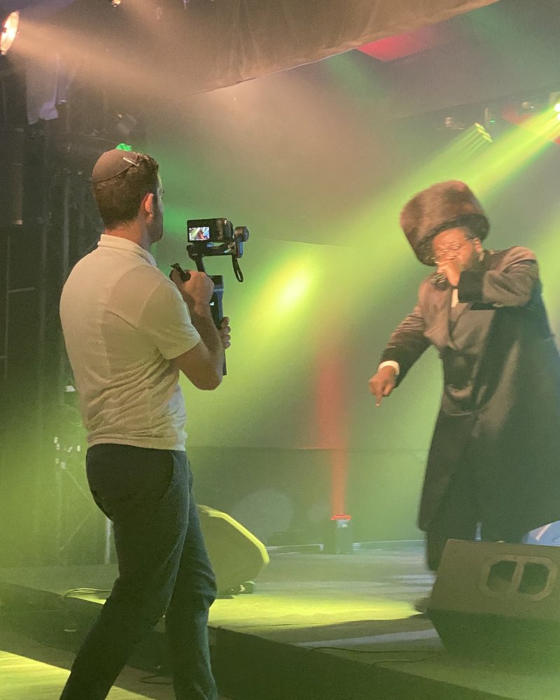 Yaakov filming a singer on stage with the camera on a gimbal, green stage light